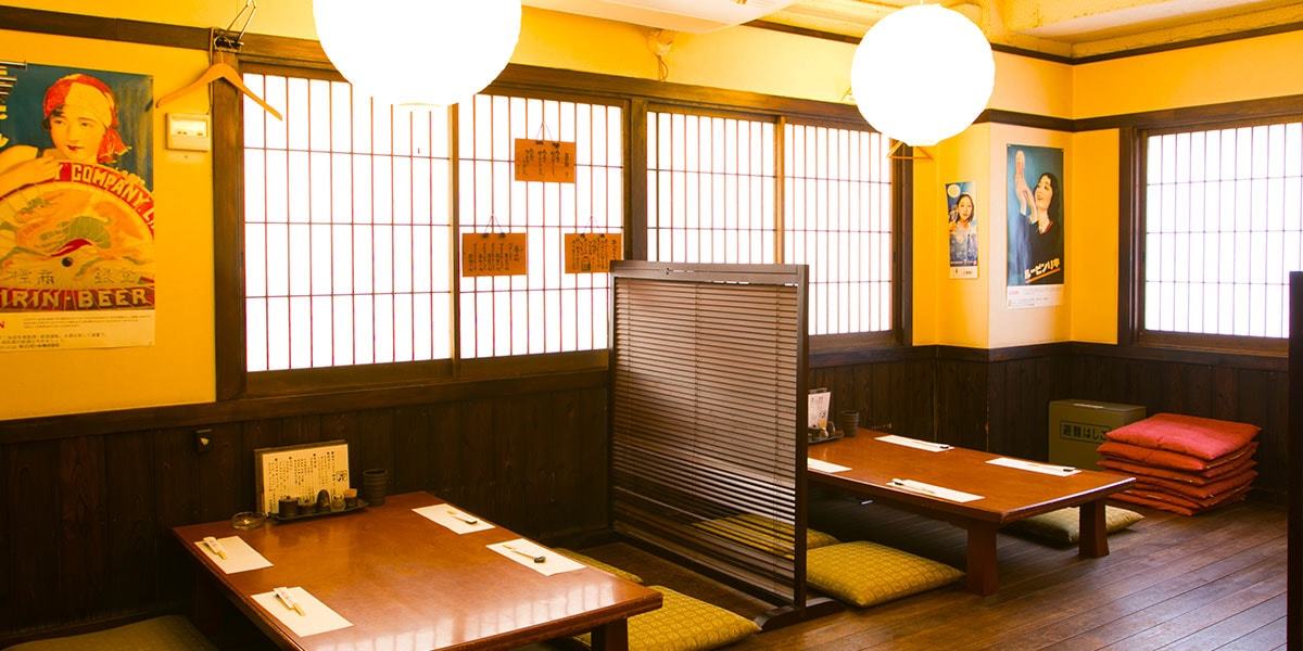 二階の座敷席の様子です。和紙を丸い提灯風にした電灯と、座布団を並べた卓席です。隣の席とは木製の小さな屏風で間仕切りしています。最大４０名ご一同でご利用いただけます。